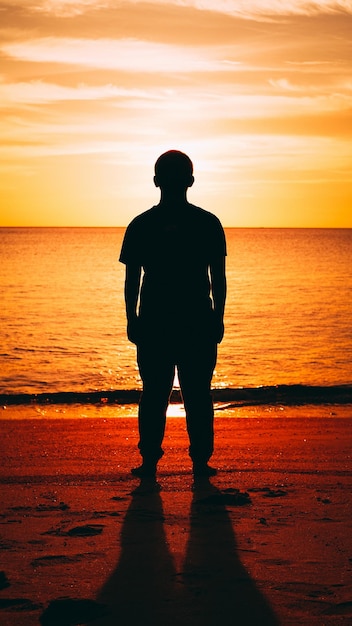 Silhouette di un uomo in piedi sulla spiaggia durante il tramonto