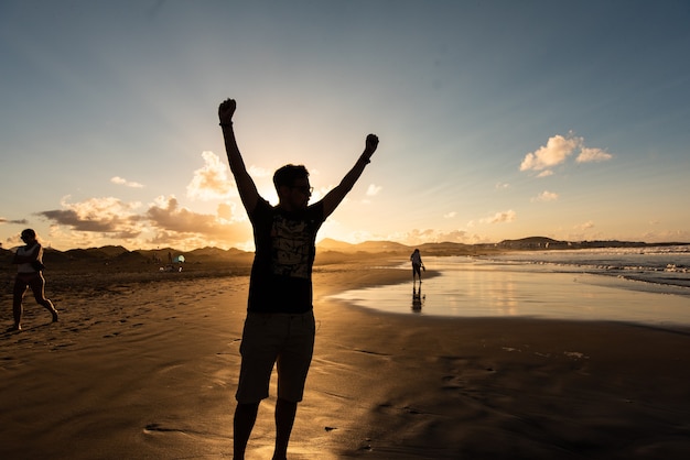 Silhouette di un uomo su una spiaggia che alza le braccia in trionfo Finalmente le vacanze estive
