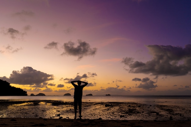 Silhouette di un uomo sulla spiaggia al tramonto. L'uomo si rallegra incontra il tramonto