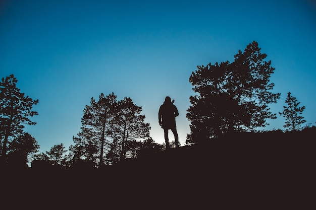 Silhouette di un viaggiatore nel mezzo di una foresta con uno zaino su uno sfondo di cielo blu
