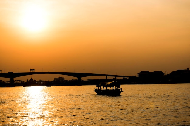 Silhouette di una barca che galleggia nell'acqua e dietro un grande ponte.