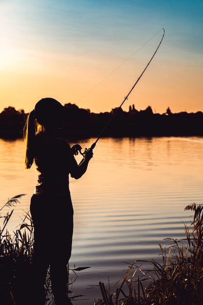 Silhouette di una donna al tramonto con una canna da pesca vicino allo stagno