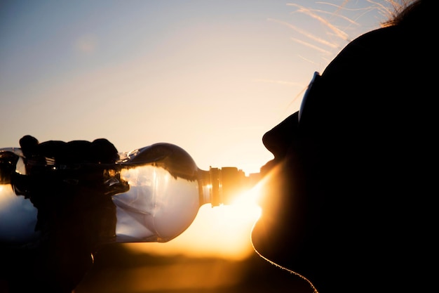 Silhouette di una donna che beve acqua al tramonto