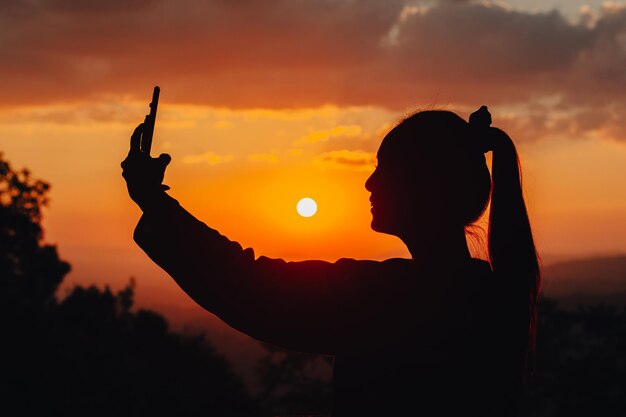 Silhouette di una donna che scatta una foto nel bel mezzo di un bellissimo tramonto sulla montagna.