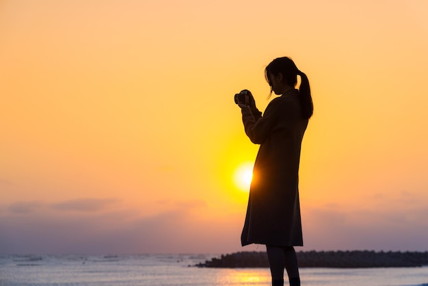 Silhouette di una donna che usa la fotocamera per scattare una foto al tramonto sulla spiaggia