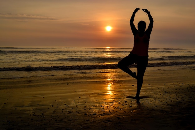 Silhouette di una donna con le braccia aperte e su un piede sulla riva di una spiaggia al tramonto