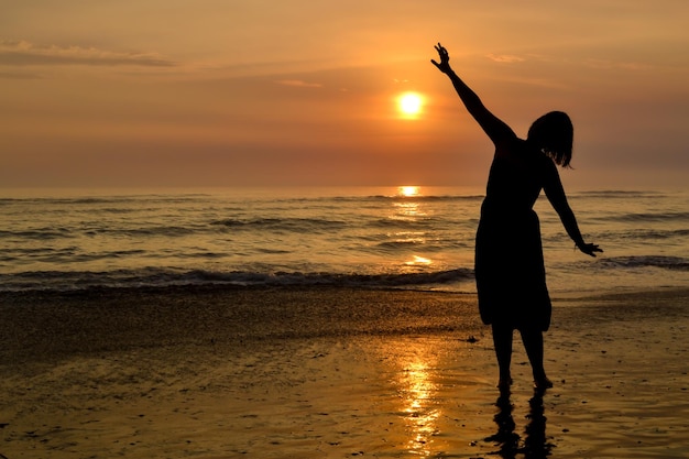 Silhouette di una donna con le braccia aperte sulla riva di una spiaggia al tramonto L'ora d'oro