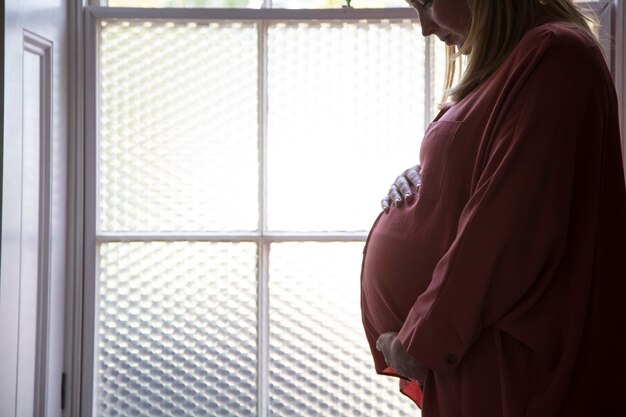 Silhouette di una donna incinta in piedi davanti a una finestra