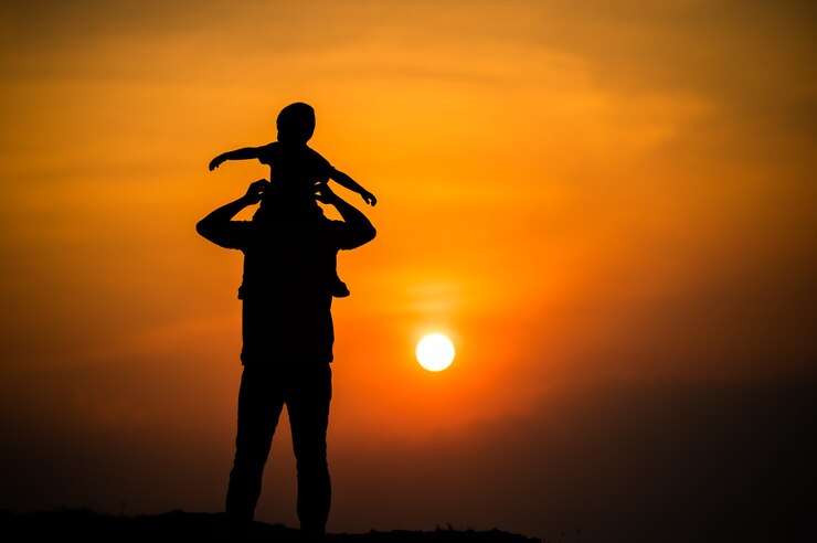 Silhouette di una famiglia con un ragazzo che cavalca felicemente il collo di suo padre contro il cielo del tramonto