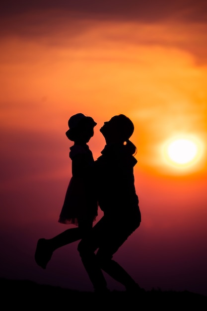 Silhouette di una famiglia con una madre felice che gioca con una ragazza nel cielo al tramonto