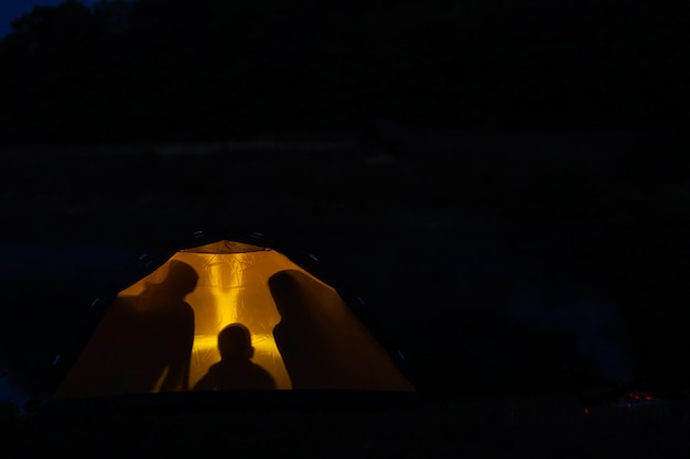 Silhouette di una famiglia in una tenda. In campeggio con la famiglia nella natura selvaggia