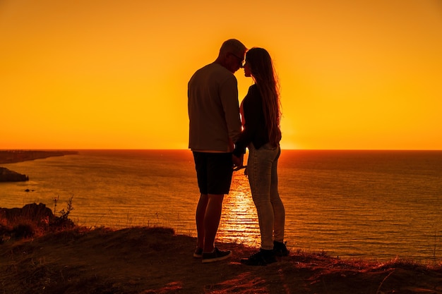 Silhouette di una giovane coppia romantica che si gode una serata su una scogliera a picco sul mare con un rosso