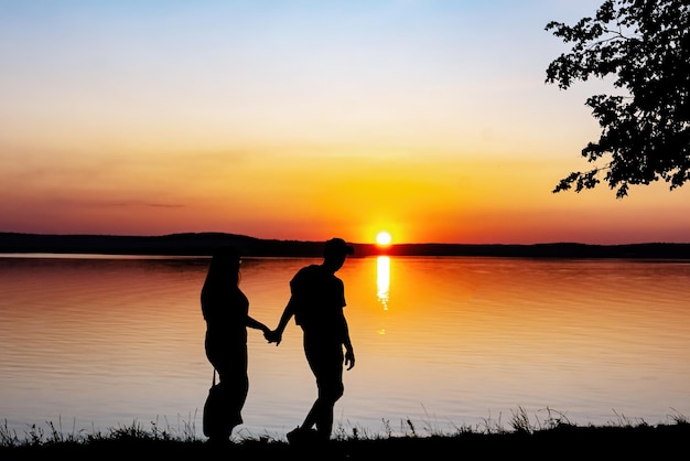 Silhouette di una giovane coppia uomo e ragazza che stanno guardando il tramonto sulla riva Sole che tramonta sull'orizzonte