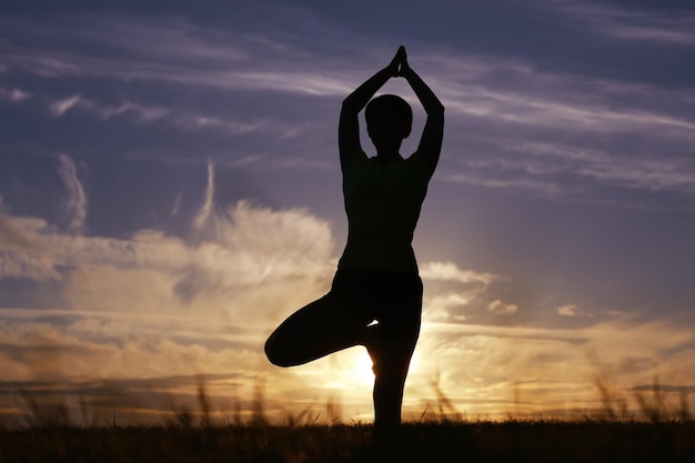 Silhouette di una giovane ragazza in postura yoga al tramonto