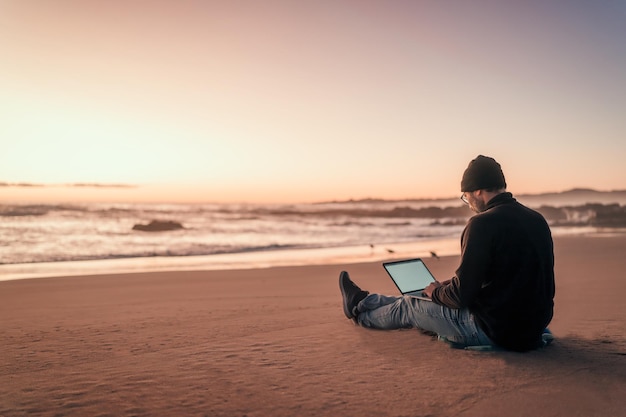 Silhouette di una persona che lavora al suo computer portatile all'aperto sulla spiaggia all'ora d'oro back viewx9