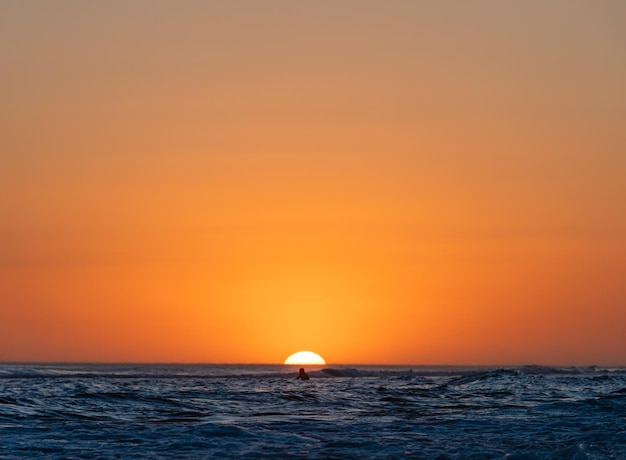 Silhouette di una persona sola in mare durante un colorato tramonto sulla spiaggia