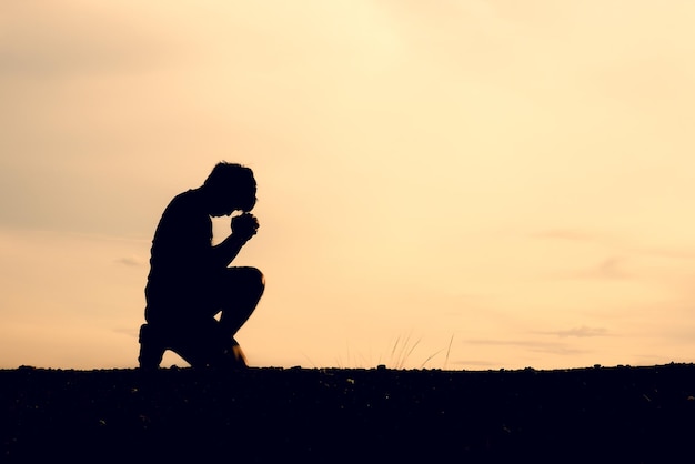 Silhouette di uomini seduti e che pregano per le benedizioni concetto di speranza