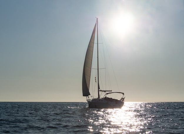 Silhouette di yacht a vela su acqua di mare incandescente al tramonto sullo sfondo