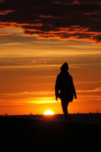 Silhouette donna che cammina sul campo contro il cielo durante il tramonto