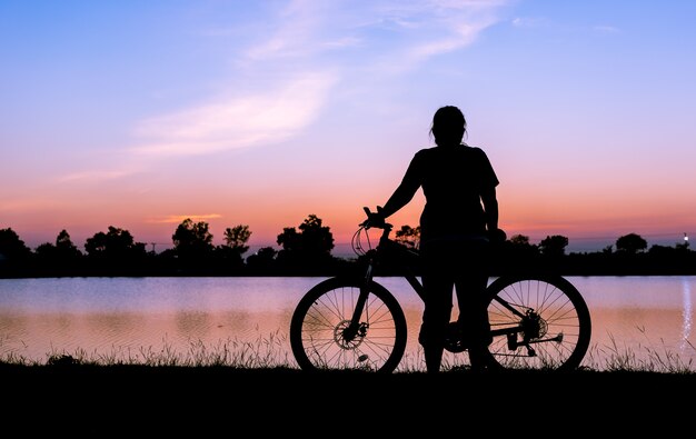 silhouette donna e bicicletta con lago sul tramonto