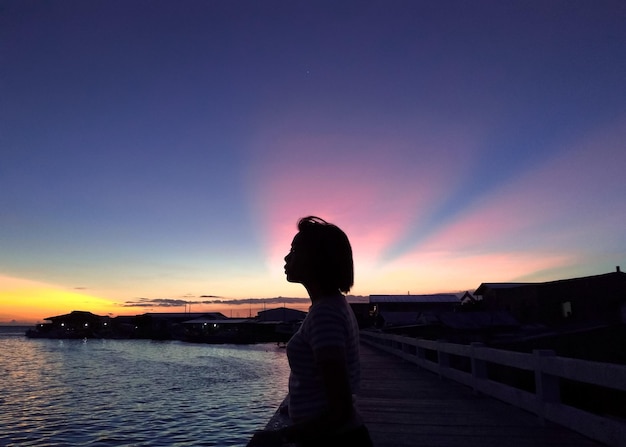 Silhouette donna in piedi sulla riva contro il cielo durante il tramonto