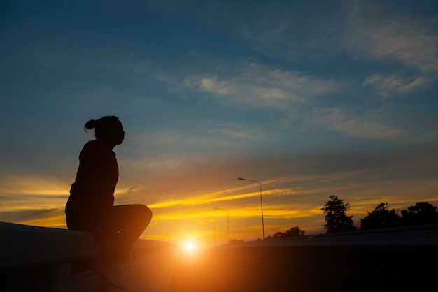 Silhouette donna sulla strada a guardare il tramonto giallo e arancione al tramonto