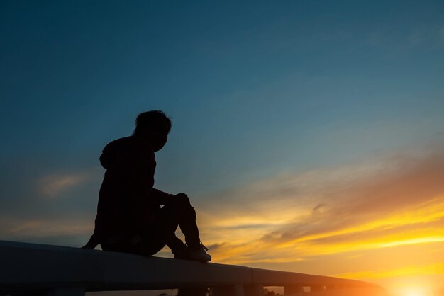 Silhouette donna sulla strada a guardare il tramonto giallo e arancione al tramonto