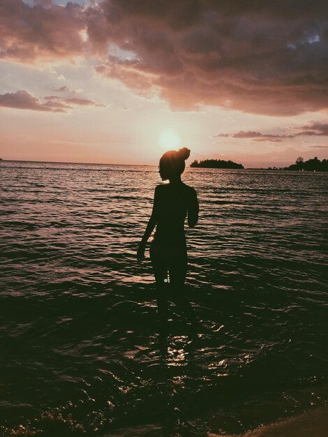 Silhouette giovane donna in piedi sulla spiaggia contro il cielo durante il tramonto