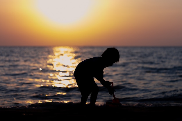 Silhouette Il ragazzo sta giocando a beach sand castle. Al tramonto Divertiti