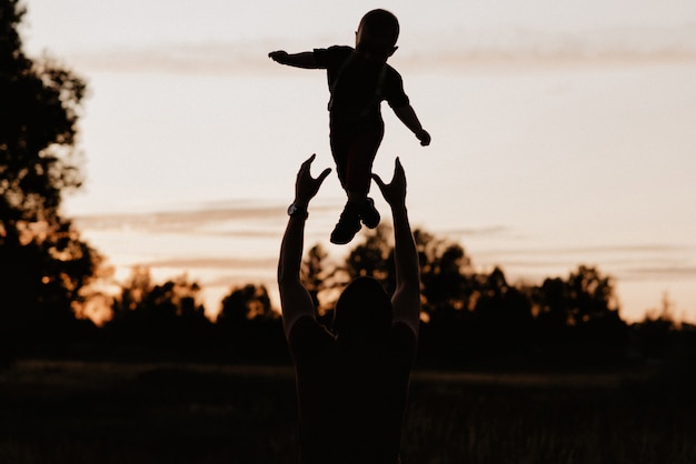 Silhouette papà vomita il suo piccolo figlio in un campo in estate al tramonto