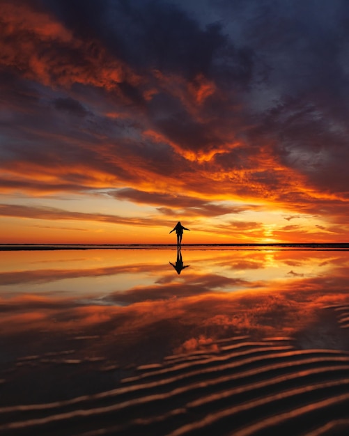 Silhouette persona su sfondo bellissimo cielo al tramonto sulla riflessione sull'oceano raggi sole in acqua