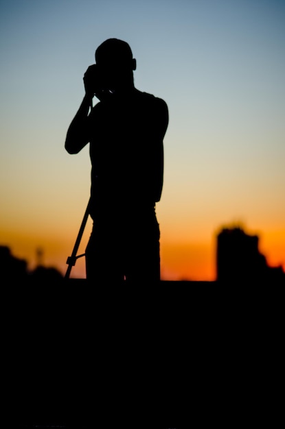 Silhouette uomo con la telecamera e in piedi contro il cielo durante il tramonto