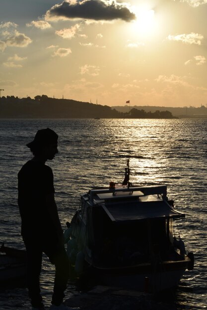 Silhouette uomo in piedi sul mare contro il cielo durante il tramonto