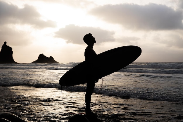 Silhuoette di un surfista in spiaggia durante il tramonto guardando il cielo