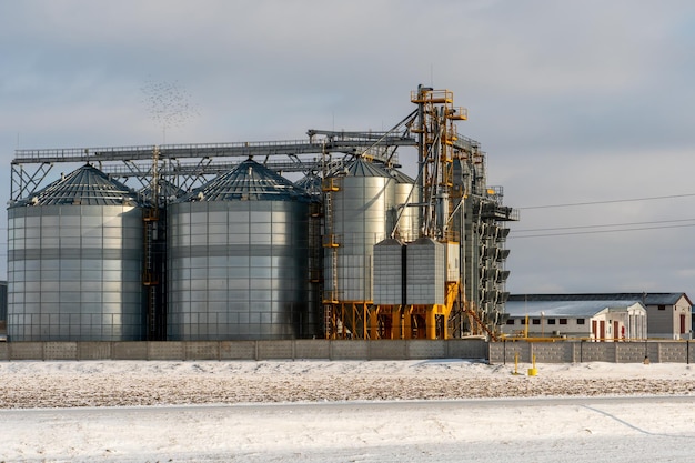 Silos d'argento contro il cielo blu in inverno Stoccaggio grano in inverno a basse temperature Produzione per la lavorazione asciugatura pulitura e stoccaggio di prodotti agricoli farina cereali e grano