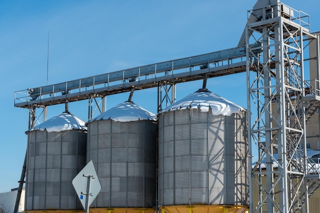 Silos d'argento su impianto di produzione agricolo per la lavorazione essiccazione pulitura e stoccaggio di prodotti agricoli farina cereali e grano Il silo del granaio dell'ascensore è coperto di neve in inverno