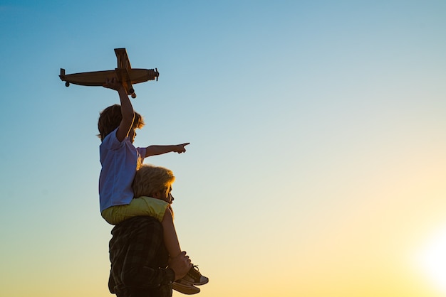 Siluetta al tramonto di padre felice e figlio del bambino con l'aeroplano sogna di viaggiare. Bambino felice del ragazzo.