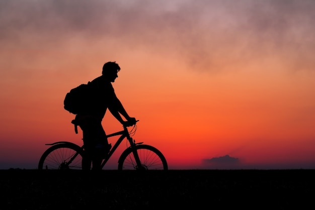 Siluetta del ciclista sullo sfondo del tramonto rosso. Motociclista con la bicicletta sul campo durante l'alba