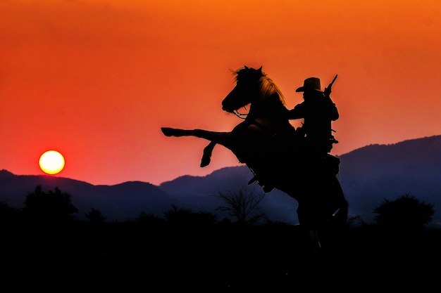 Siluetta del cowboy su un cavallo durante il tramonto piacevole