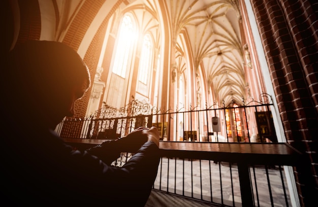 Siluetta del giovane che prega in chiesa alla luce del sole