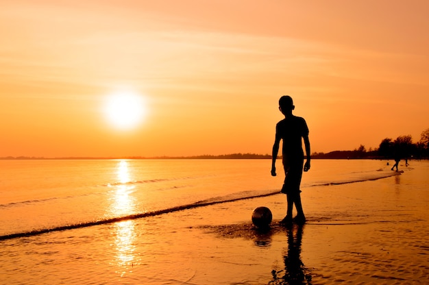 Siluetta del ragazzo che gioca a calcio sulla spiaggia