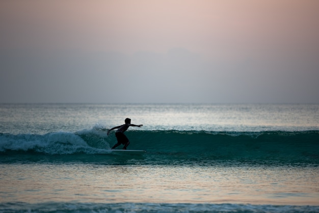 Siluetta del ragazzo che pratica il surfing a bordo in riva all'oceano durante il tramonto