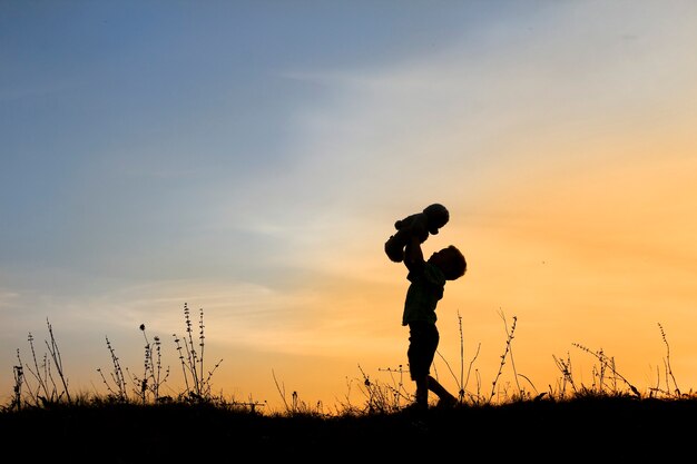 Siluetta del ragazzo del bambino con l'orso sul tramonto