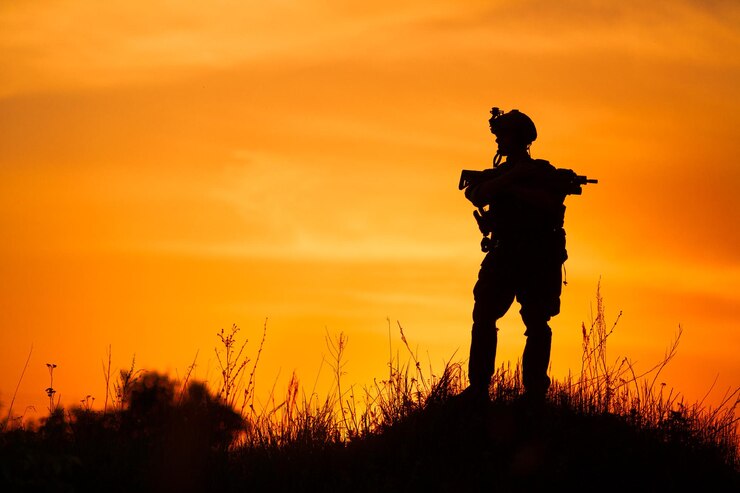 Siluetta del soldato militare o dell'ufficiale con le armi al tramonto