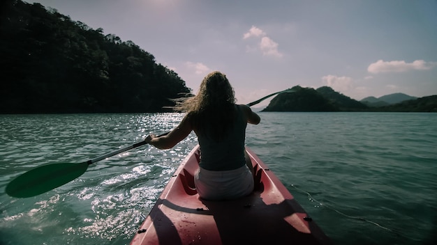 Siluetta del turista della donna che alza le mani durante la navigazione in canoa lungo l'acqua della baia del mare