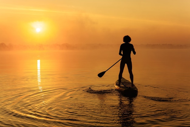 Siluetta dell'uomo che galleggia a bordo del sup sul lago nebbioso