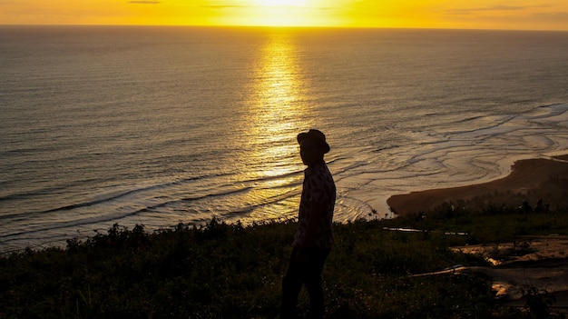 Siluetta dell'uomo che indossa cappello sullo sfondo del sole che tramonta nell'oceano