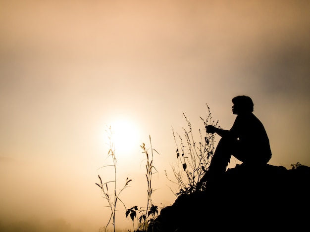 Siluetta dell'uomo che si siede su una scogliera all'alba.