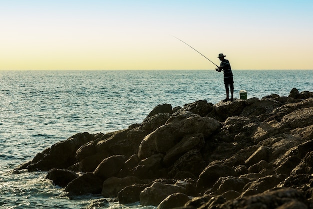 Siluetta dell'uomo di pesca al tramonto. Persone che si godono l'hobby del fine settimana durante le vacanze.