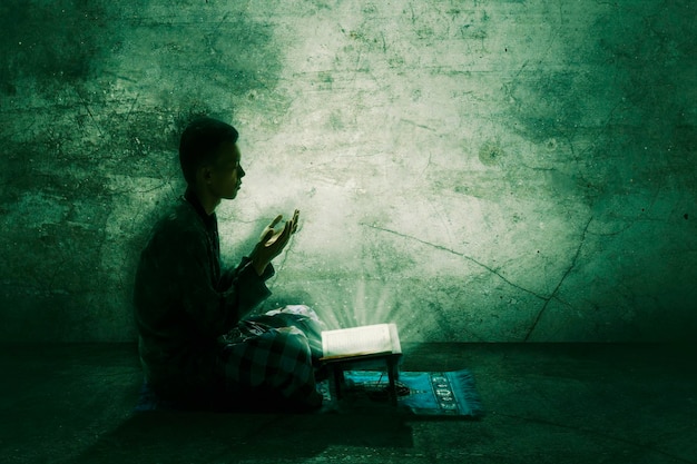 Siluetta dell'uomo musulmano devoto che prega Allah dopo aver letto il Corano